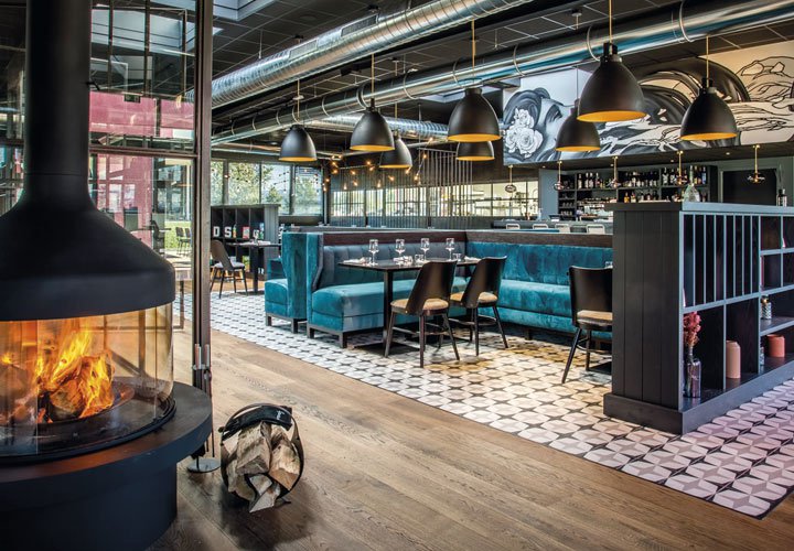 Dining room of a restaurant with blue sofas, a mural in the background and a glassed-in fireplace in the foreground